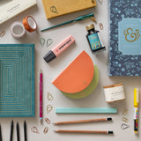 Stationery Flatlay including half moon notepads and a suedette notebook.