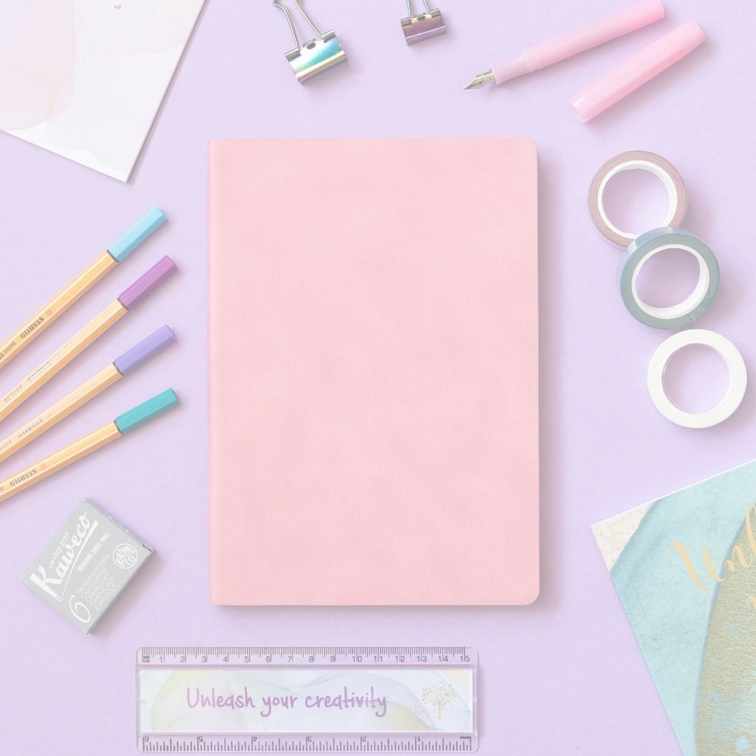 Pink notebook with stationery items on a light purple background