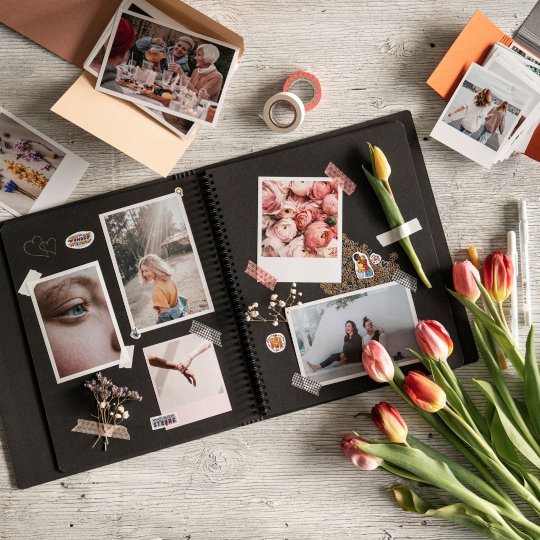 Open photo album with printed photos and flowers on a wooden surface