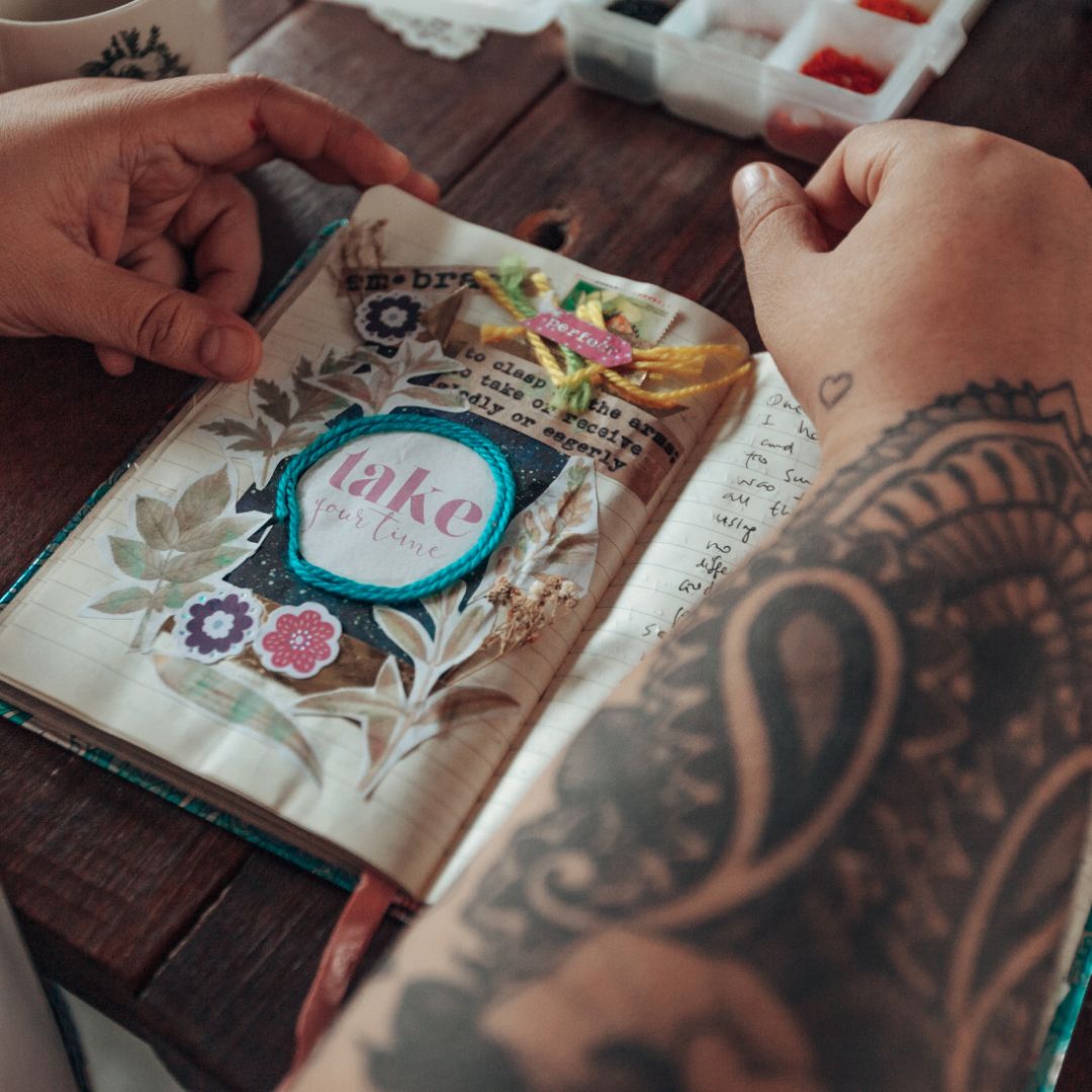 Person with tattooed arm holding a decorated book on a wooden surface