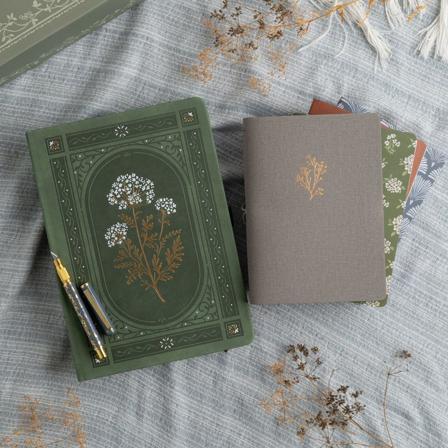Two notebooks with floral designs on a textured surface with dried flowers.